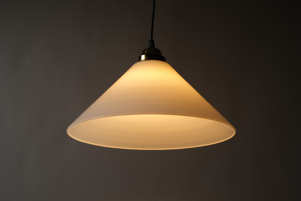 Front illuminated view of a 1980s vintage opal glass cone pendant lamp, showing the warm downward and outward glow cast through the opaline glass cone against a dark background.