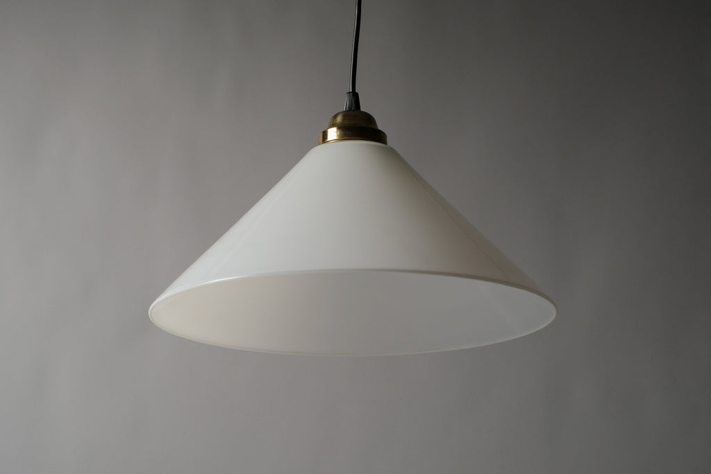 Low-angle front view of a 1980s vintage opal glass cone pendant lamp unlit, showing the broad flared conical silhouette and ivory white opaline glass surface suspended on a black cord.