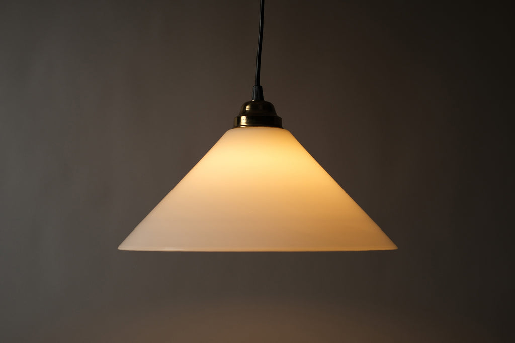 Profile illuminated view of a 1980s vintage opal glass cone pendant lamp, showing the warm amber glow radiating through the opaline glass cone and the clean conical silhouette when lit.