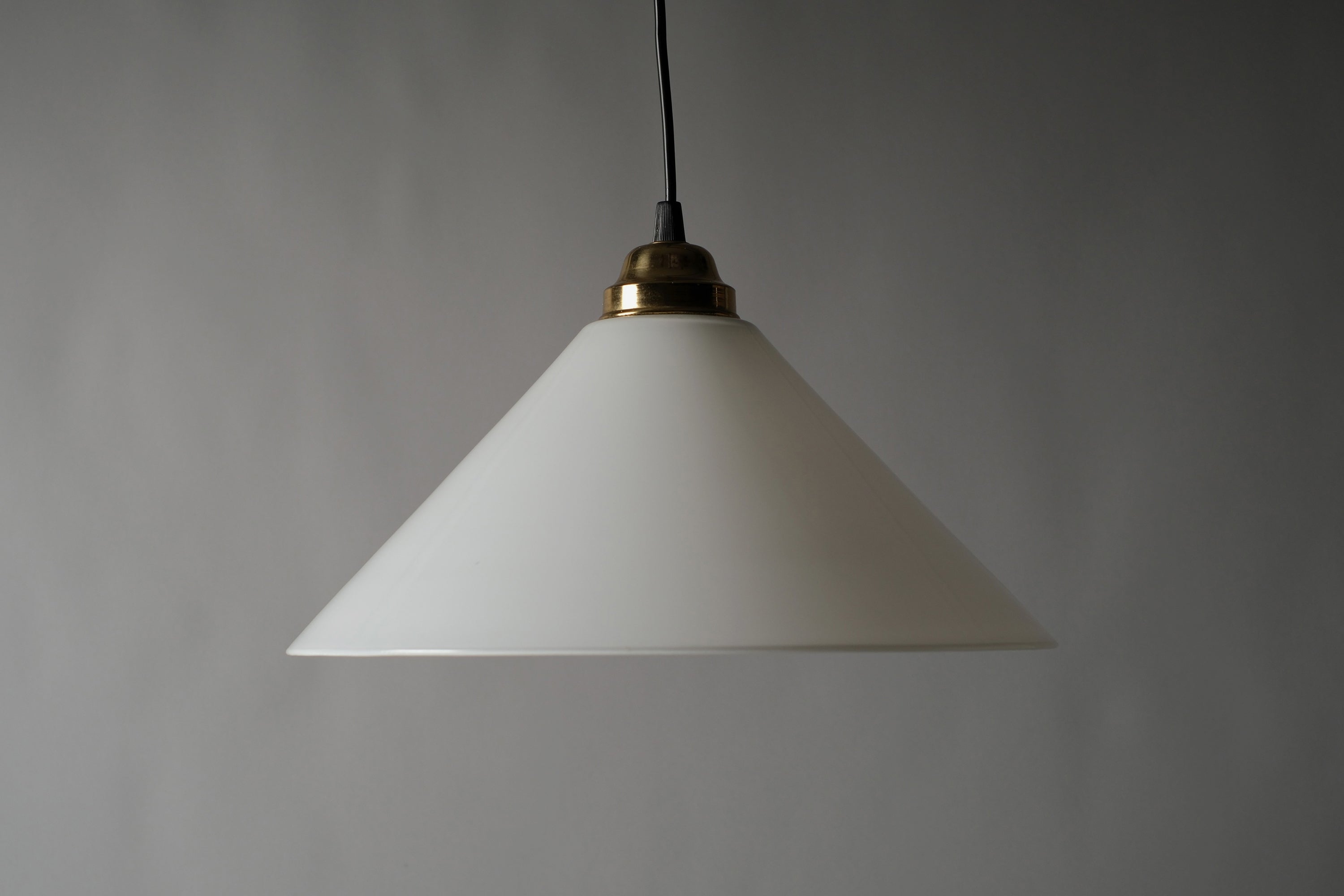 Profile view of a 1980s vintage opal glass cone pendant lamp, showing the clean conical silhouette and gold-plated brass fitting against a neutral grey background.