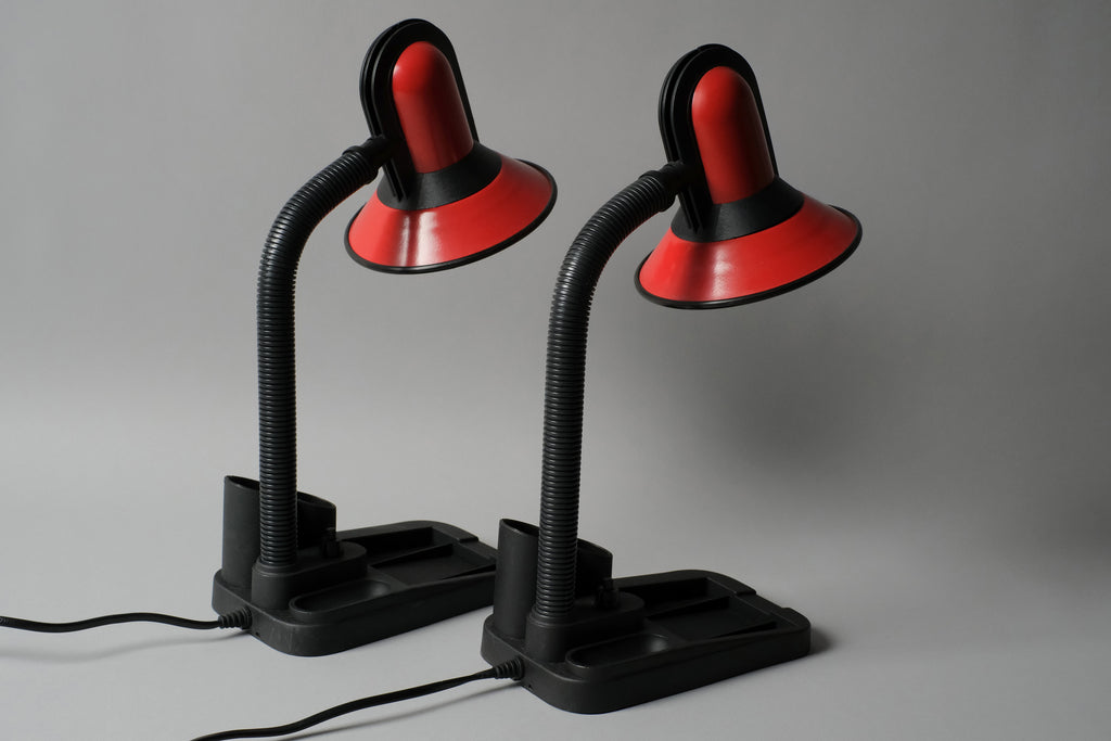 Rear perspective image of a pair of vintage 1980s gooseneck desk lamps with built-in stationary caddies by Fase Spain. The lamps have a black plastic base with red metal dome shades with black plastic detailing.