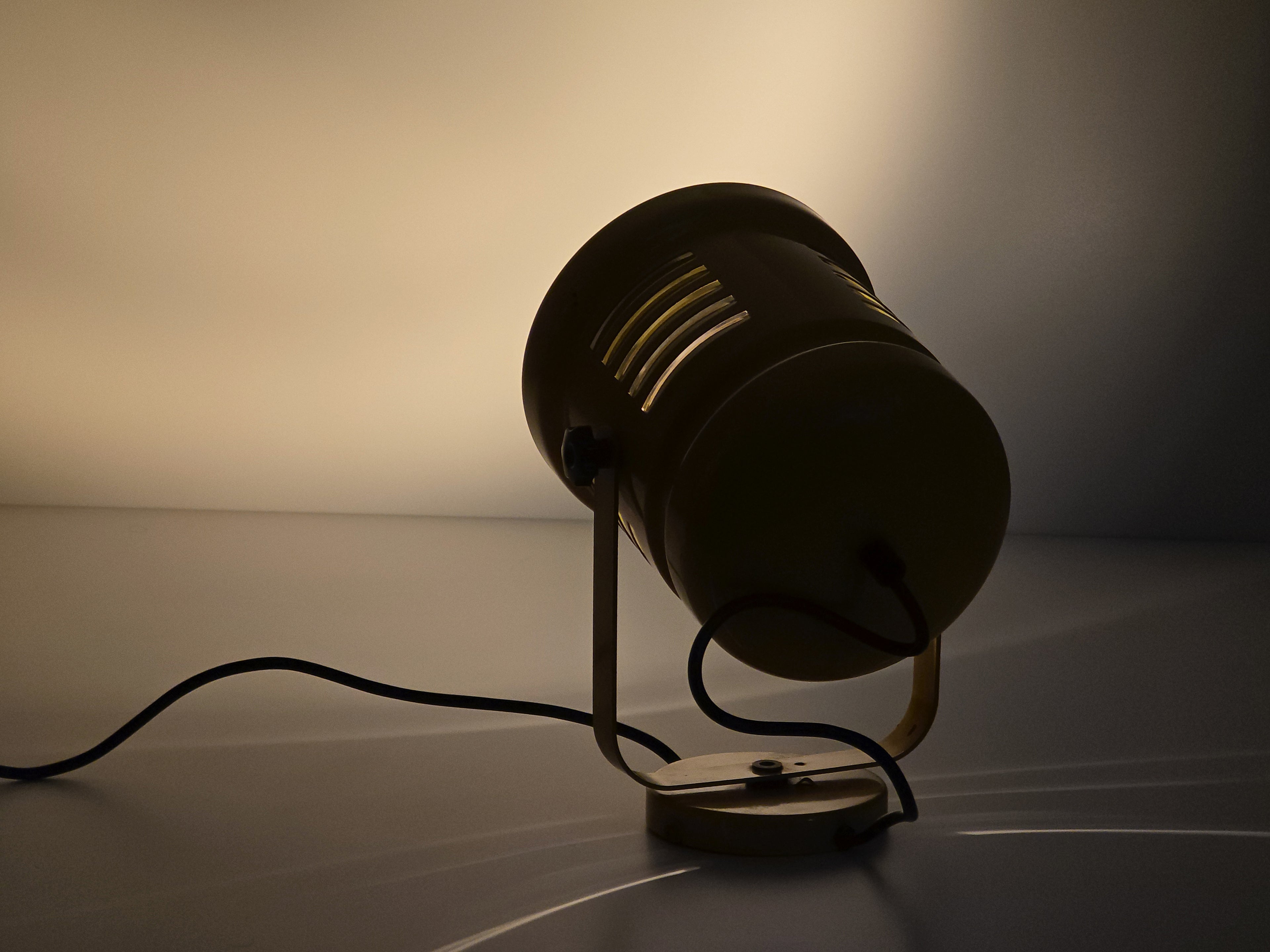 Rear view of wall lamp, lit in the dark and light projected on a neutral wall.